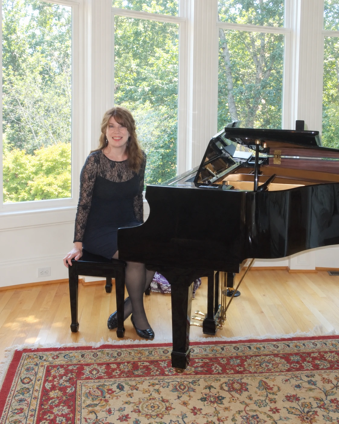 Jenny smiling beside her grand piano at home