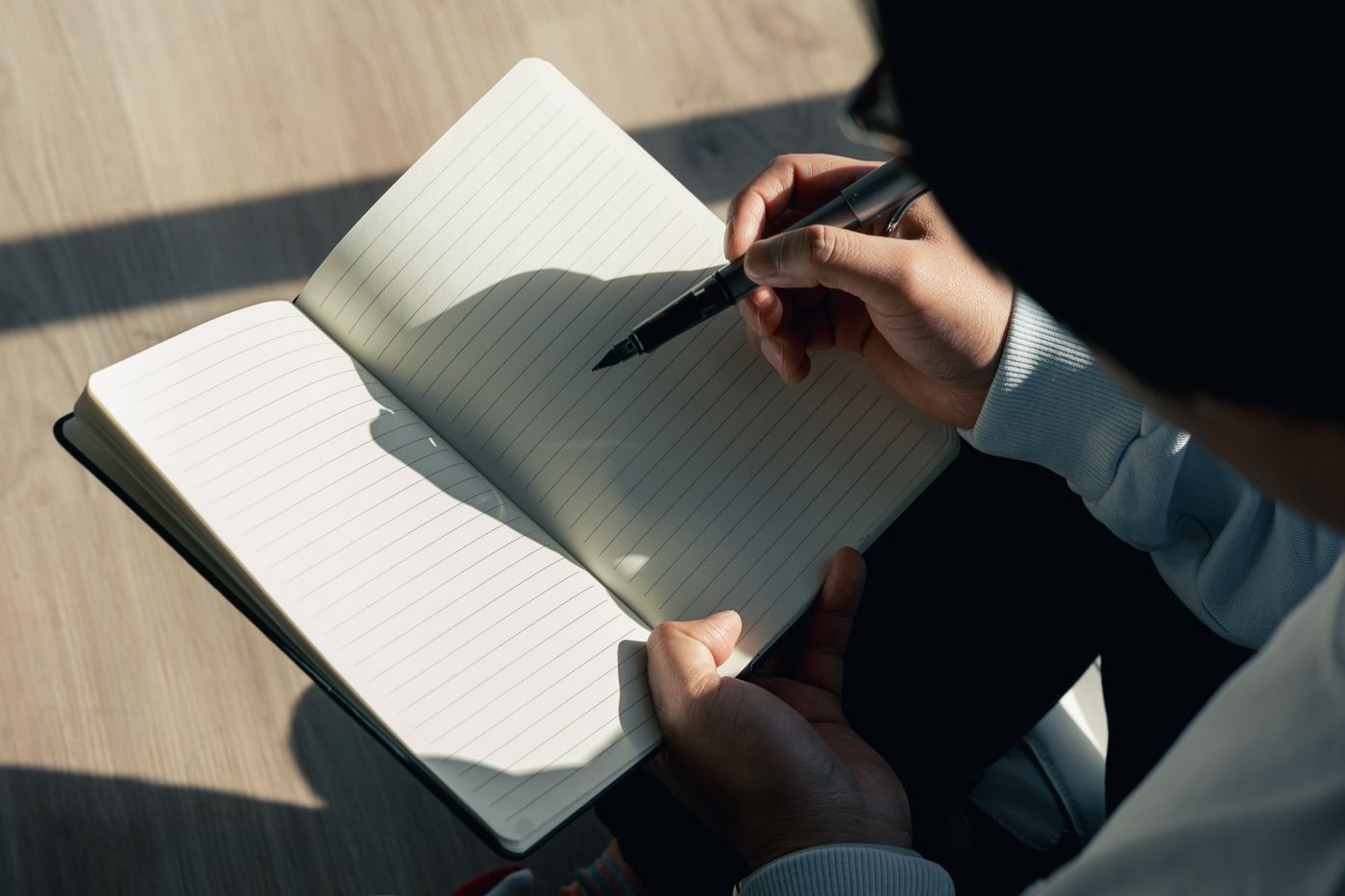 A person writing in a notebook in warm sunlight