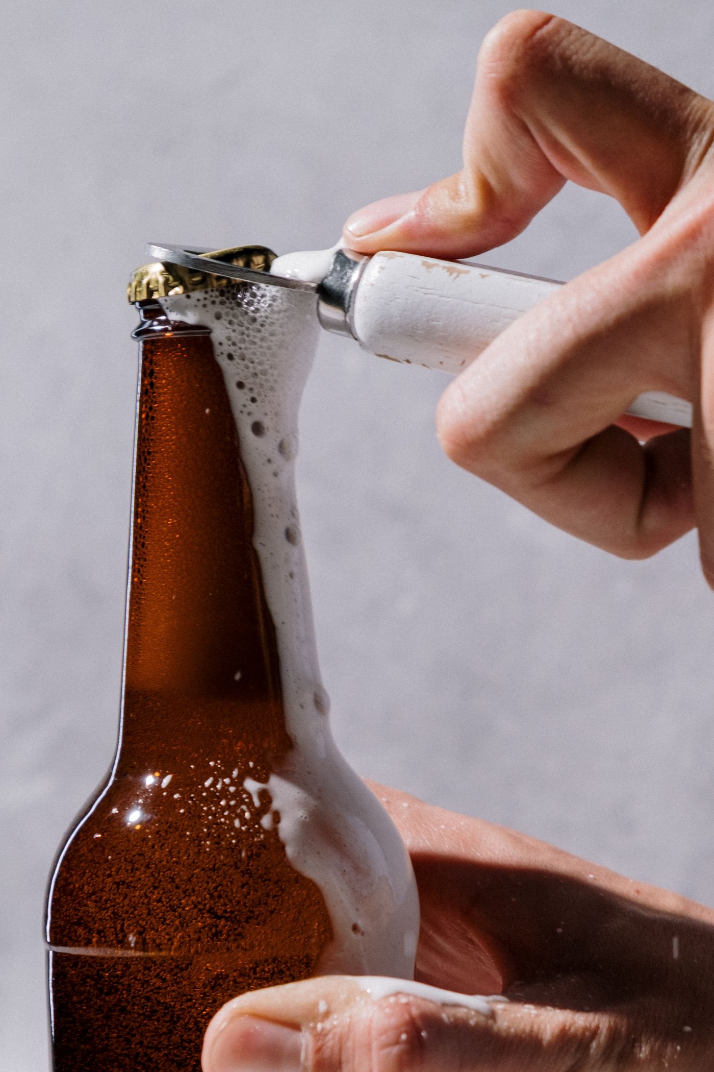 Hands opening a brown glass bottle with a bottle opener