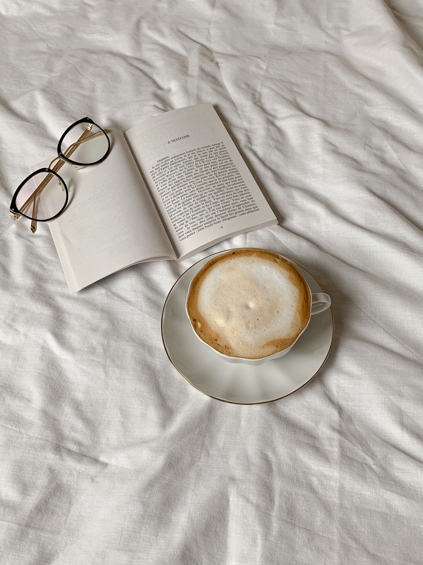 Reading glasses resting on an open book beside coffee