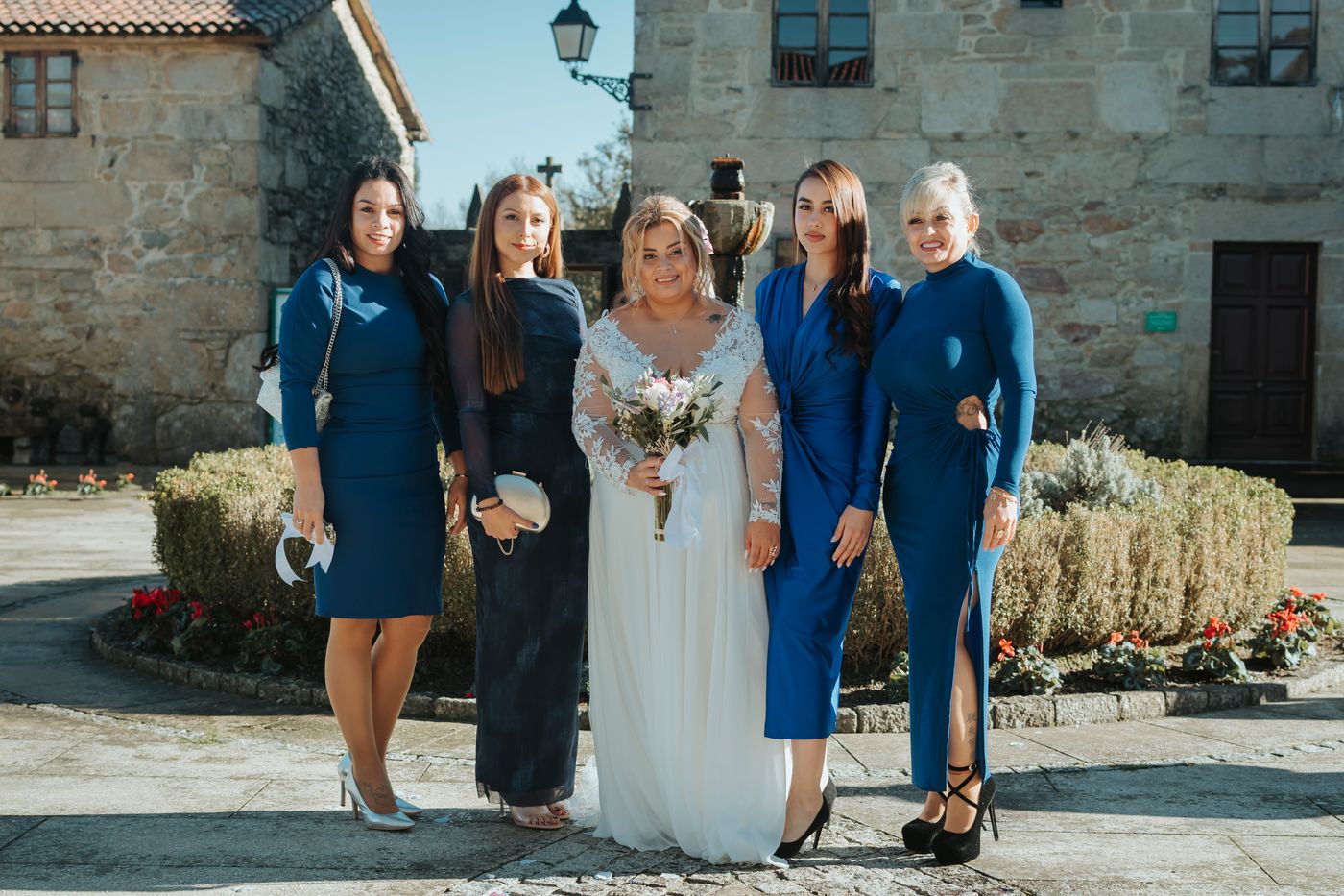 A bride and bridesmaids in blue dresses holding flowers outdoors