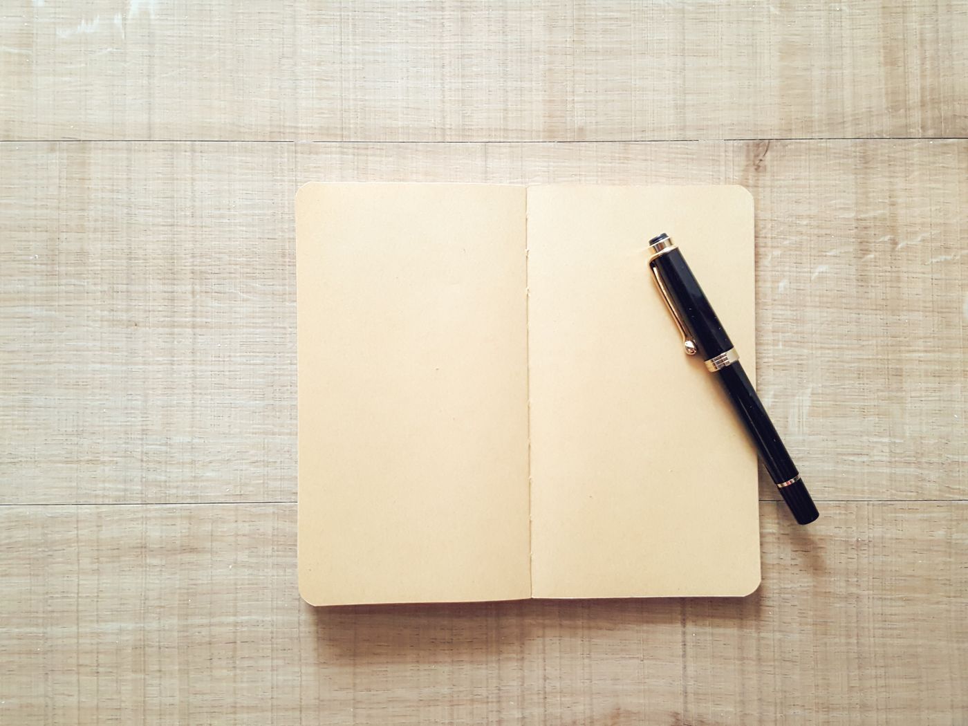 An open notebook and a black pen on a wooden surface